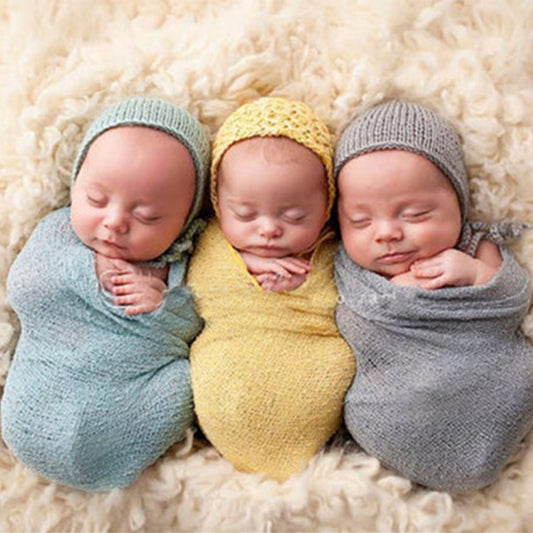Three newborn babies wrapped in colourful, soft blanket wraps in blue, yellow, and grey, lying peacefully on a fluffy cream background. | Everything Amazing Shop